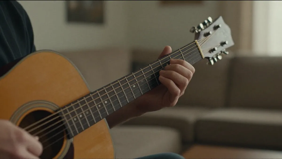 Bàn tay trái bấm dây trên cần đàn guitar, một ngón vừa nhấc khỏi phím